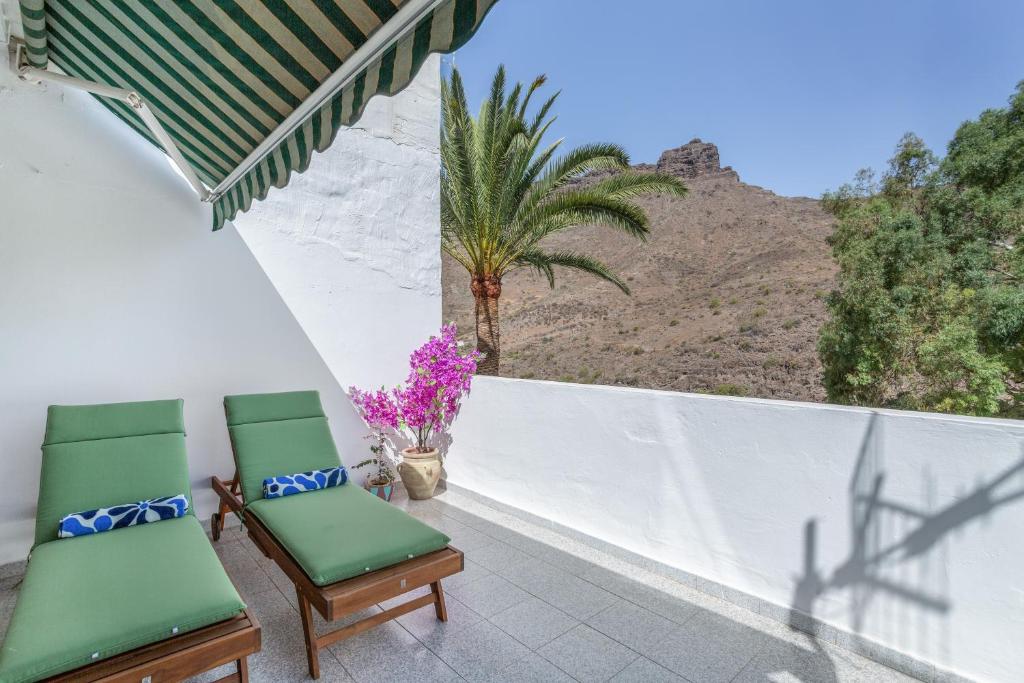 two green chairs on a balcony with a palm tree at Apartamento Danoe 5 in Mogán