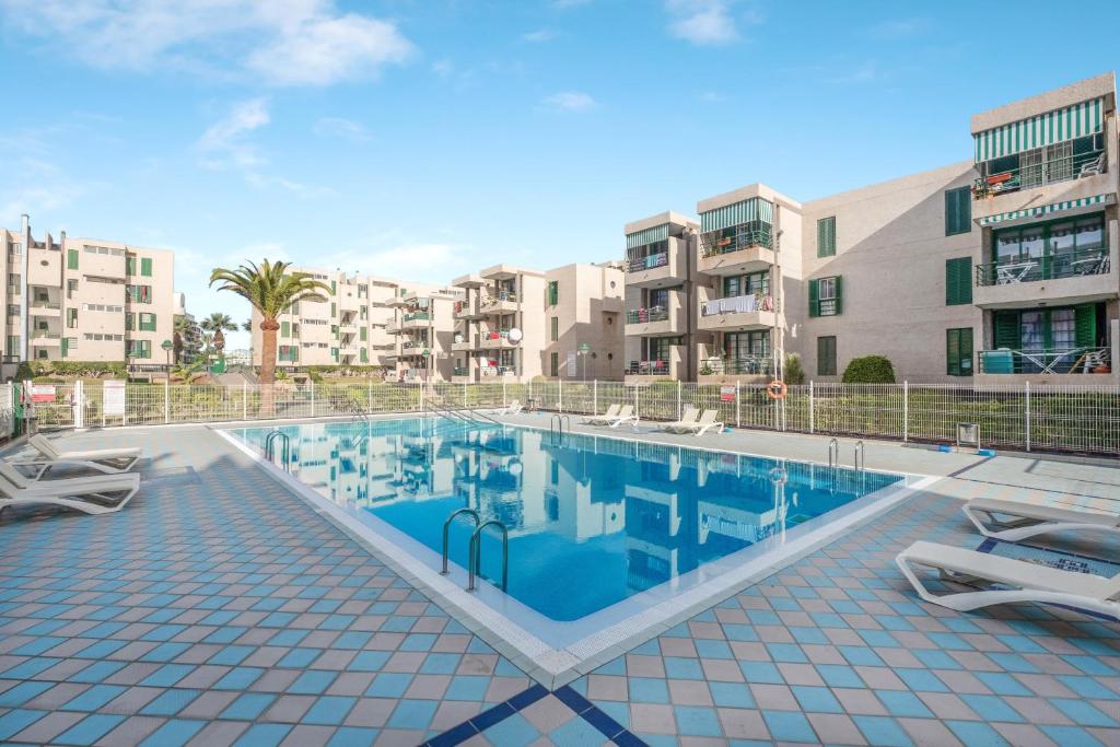 a swimming pool with two chairs and some buildings at La Casa De Enzo in Playa de las Americas