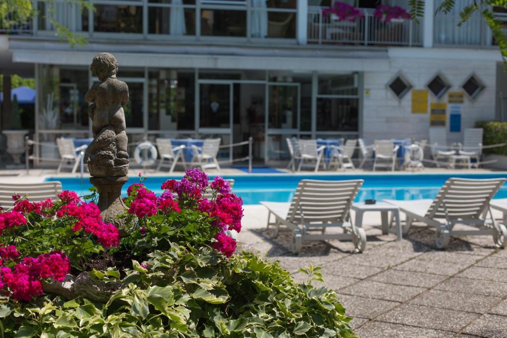 posąg przed basenem z kwiatami i krzesłami w obiekcie Hotel Gioiello w Cesenatico