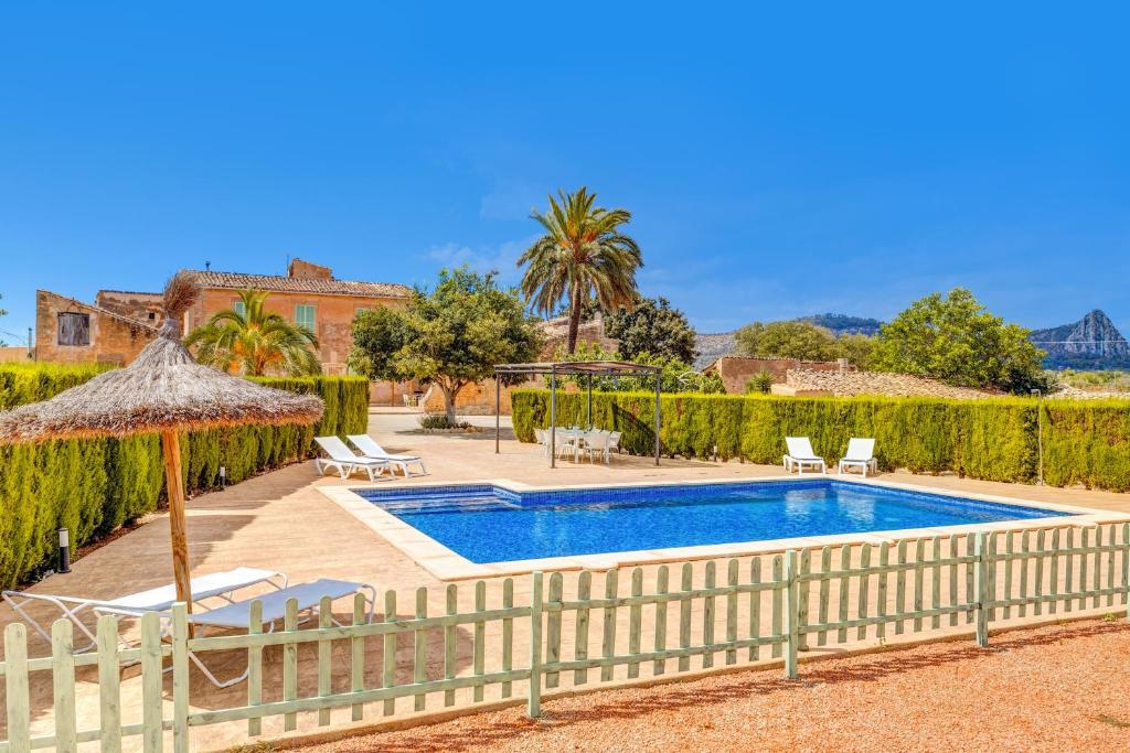 a swimming pool with a umbrella and chairs and a house at Finca Buniferri in Llucmajor