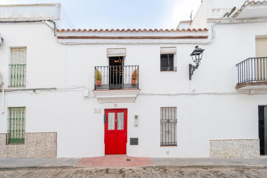 a white building with a red door and a balcony at Preciosa Casa el Pedroso in El Pedroso