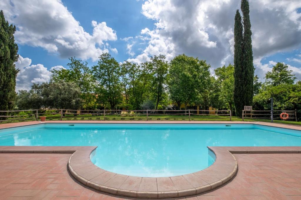 a large swimming pool with a brick patio and trees at Rosaspina - Appartamento 3 in Capalbio