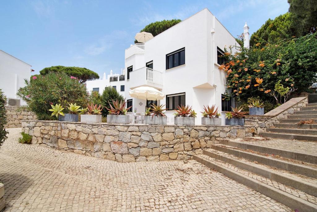 a white house with potted plants on a stone wall at Casa Harlequin in Vale do Lobo