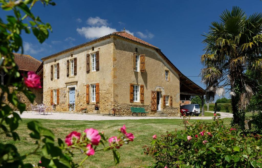 a large stone house with a palm tree and flowers at Le Guitou de Monlezun in Monlezun
