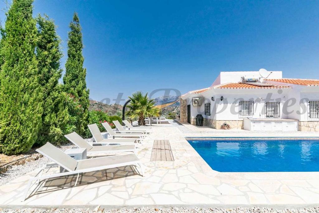a row of white lounge chairs next to a swimming pool at Casa Arco Iris in Cómpeta