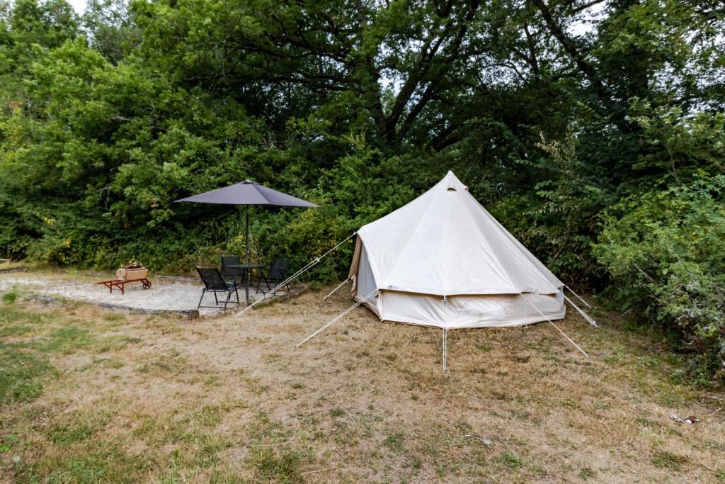 a white tent and a table and umbrella at Tente Glamping Éco-Chic in Auriac-du-Périgord