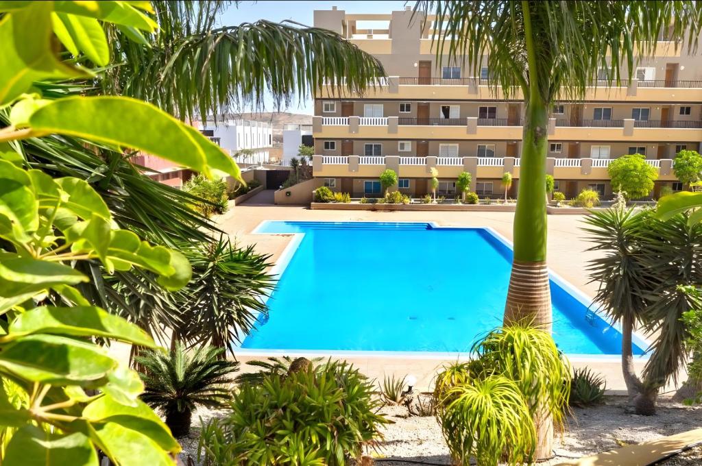a swimming pool in front of a building with palm trees at Sandra La Perla in El Médano
