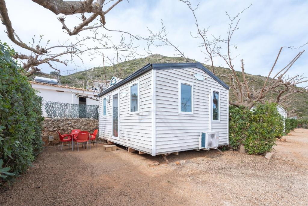a white tiny house with red chairs in a yard at Falaguera Bungalow 1 in Bárig