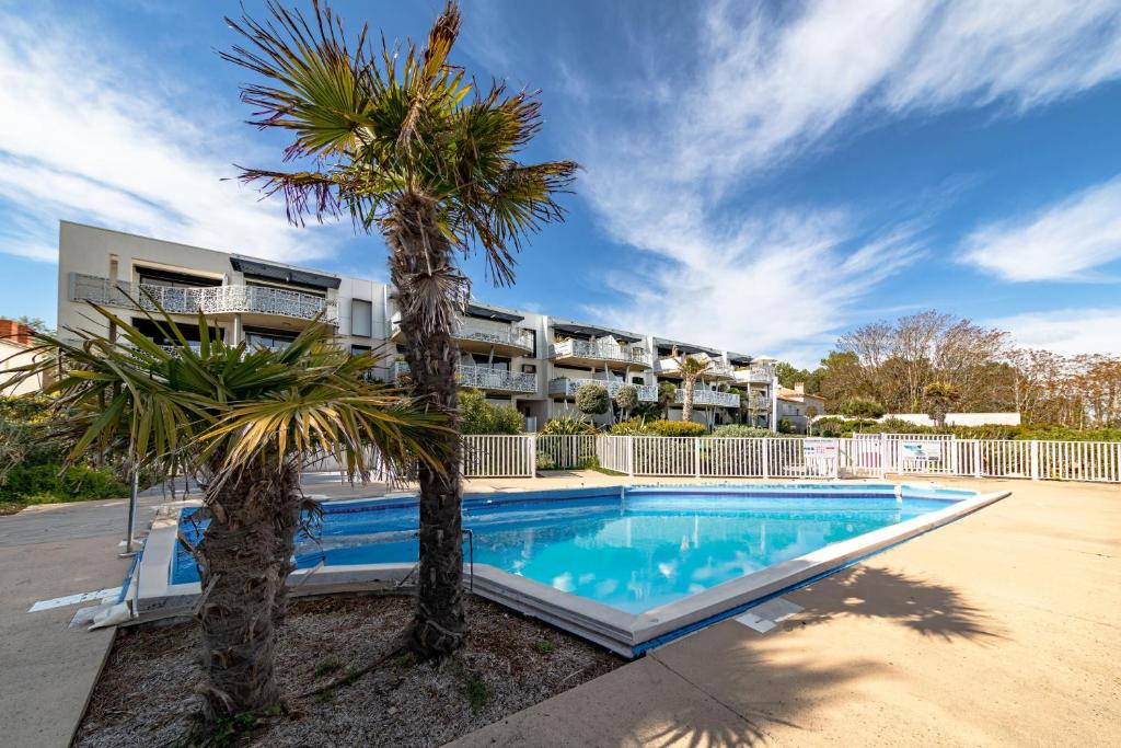 a swimming pool with palm trees in front of a building at Le Rêve 210 in La Tranche-sur-Mer