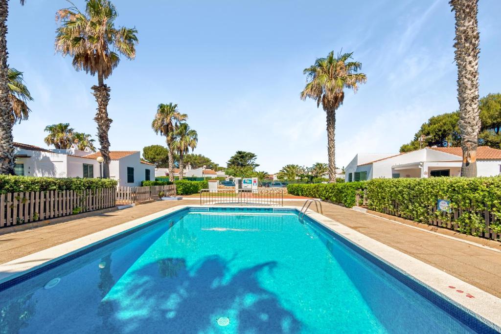 a swimming pool with palm trees in the background at Sa Calma House in Cala en Bosc