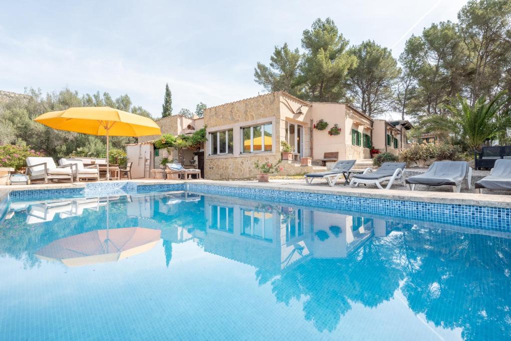 a swimming pool with an umbrella and chairs and a house at Casa Vista Monte in Llucmajor