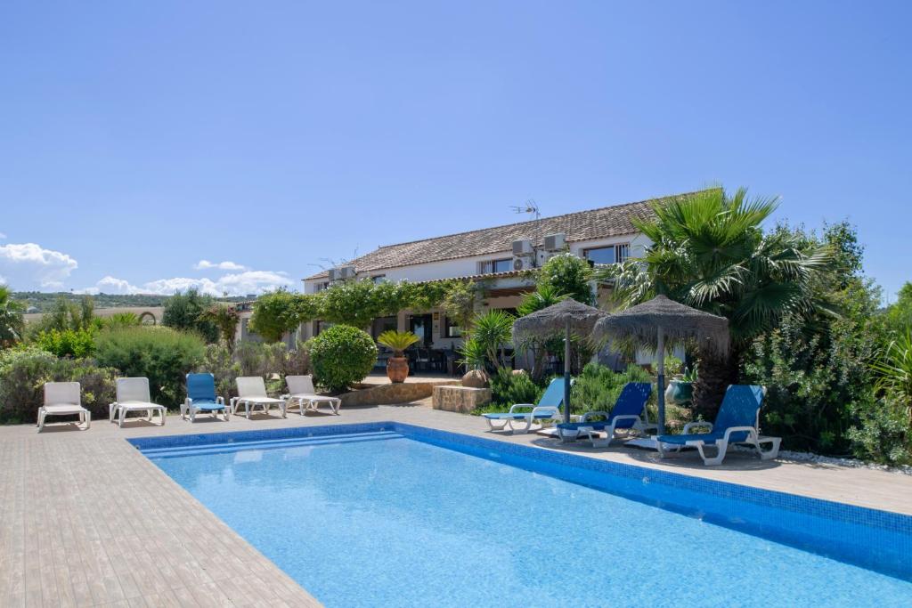 a pool with chairs and umbrellas next to a building at Finca encanto in Arcos de la Frontera
