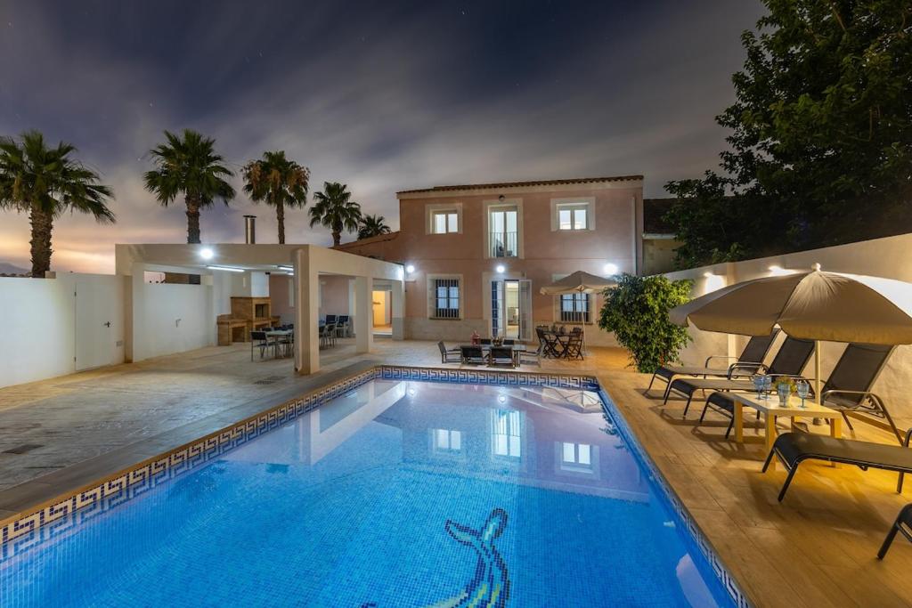 a swimming pool with tables and umbrellas next to a house at Blue Haven by Fidalsa in Catral