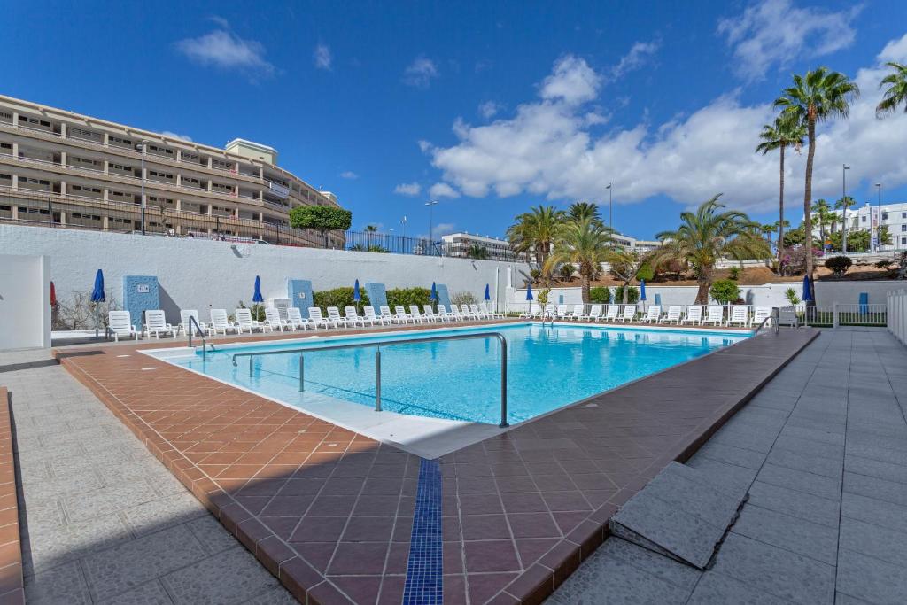 a swimming pool with chairs and a building at Apartamento Yumbo Maspalomas in Maspalomas