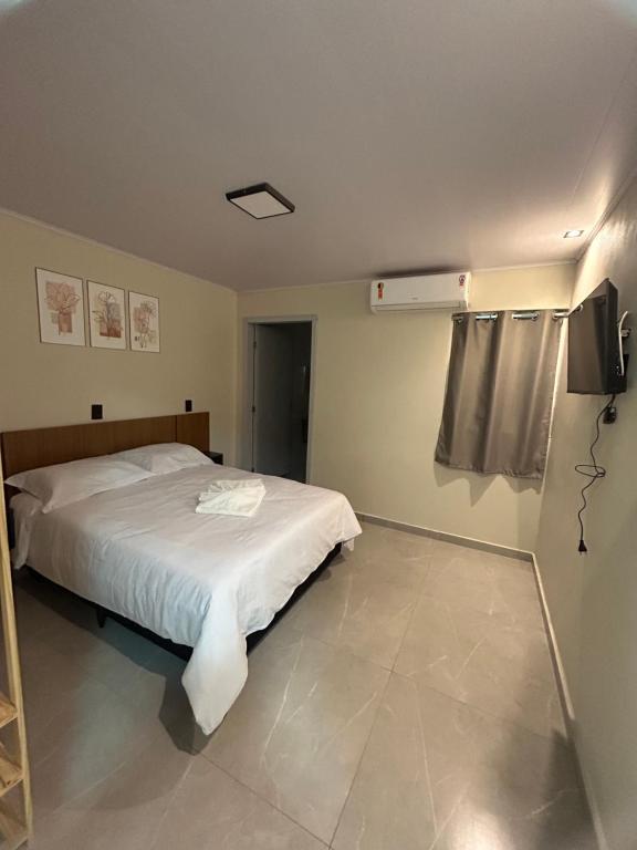 a bedroom with a white bed and a tv at Castilhos Hotel in Barracão