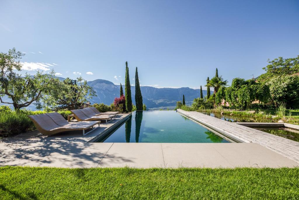 a pool with chairs and trees and mountains in the background at Kraidlhof Designapartment Veronika in Cortaccia