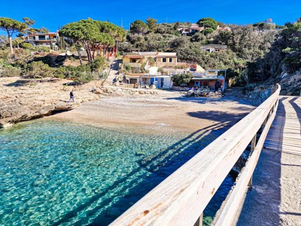 a wooden bench next to a beach with houses at Villa Galatea La Conchiglia in Capoliveri