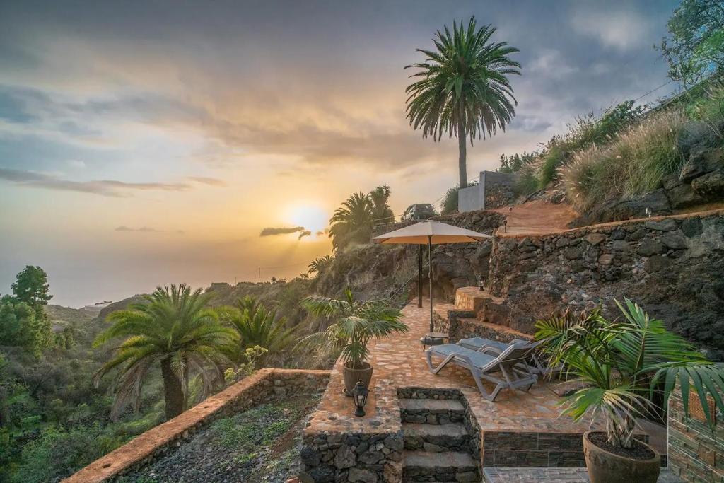 a patio with a table and an umbrella and palm trees at Cueva El Desvelo in Tijarafe
