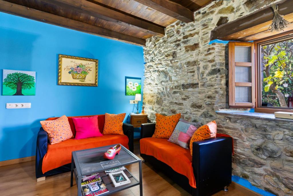 a living room with two orange chairs and a stone wall at Teixo in Vega de Logares