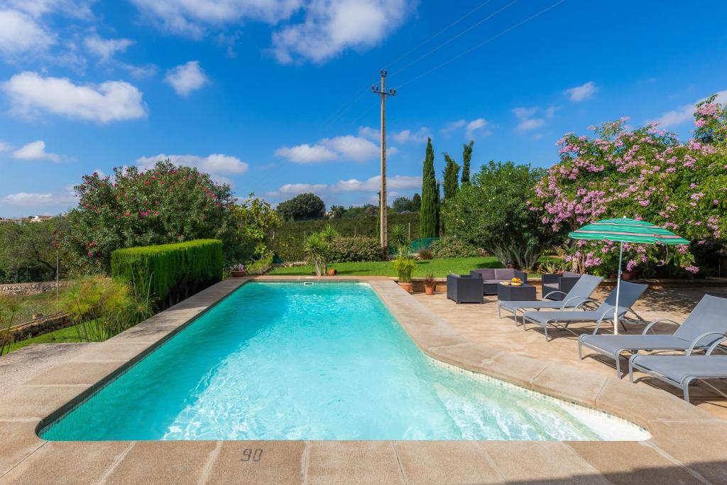 a swimming pool with chairs and an umbrella at Ses Serres in Santanyi