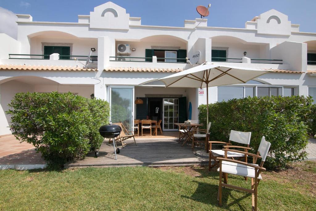 a white house with an umbrella and a grill at Casa do Ouriço - Cabanas Tavira in Tavira