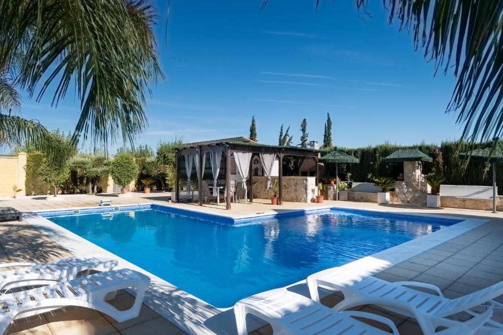 a swimming pool with chairs and a gazebo at Villa Oasis in Lora del Río
