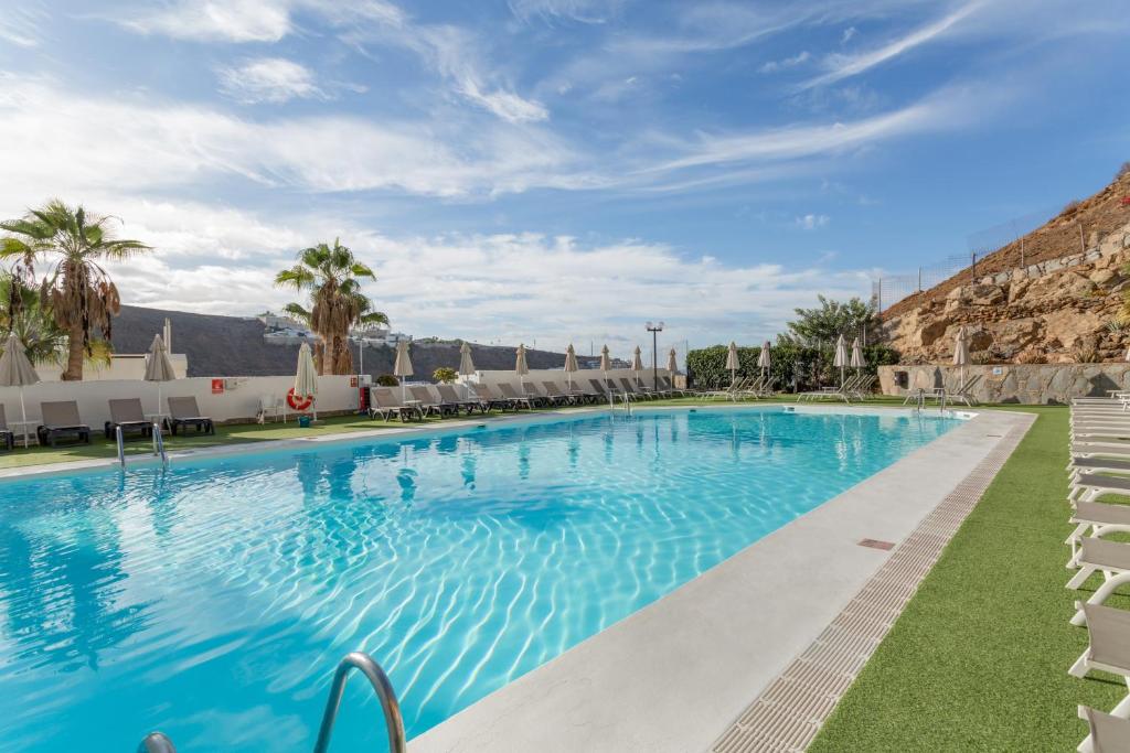 a large swimming pool with chairs and palm trees at Casa Orballo in Mogán