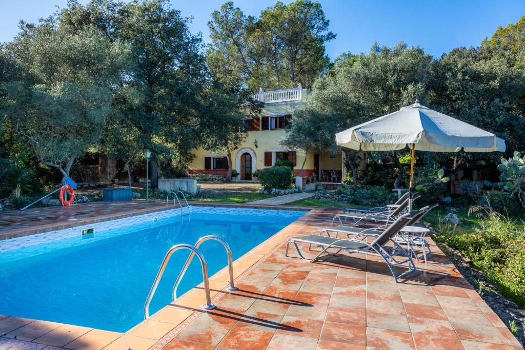 a pool with chairs and an umbrella next to a house at S' Alzina in Sencelles