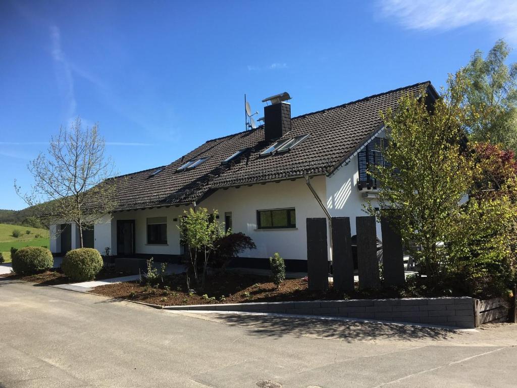 a white house with a black roof on a street at Ferienwohnung Am Holing in Bischoffen