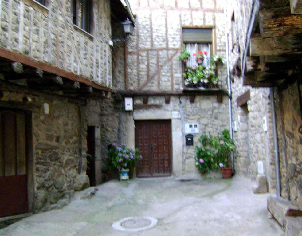 an old stone building with a red door and flowers at Casa Lopez San Martín in San Martín del Castañar