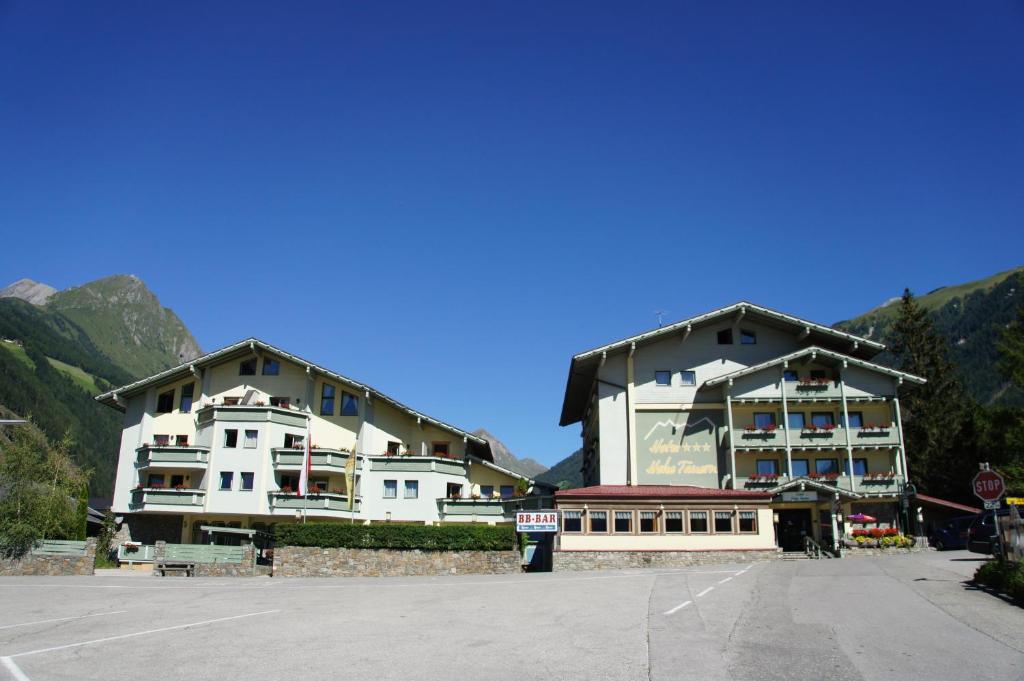 two large buildings in a parking lot with a stop sign at Hotel Hohe Tauern in Matrei in Osttirol
