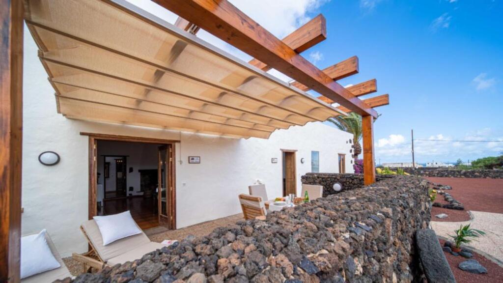 a patio with a stone wall and a wooden pergola at Casa Margarita 2 in Mala