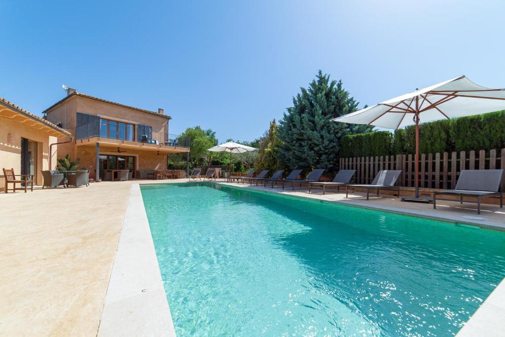 a swimming pool with chairs and an umbrella next to a house at S'hort des Frares in El Palmer