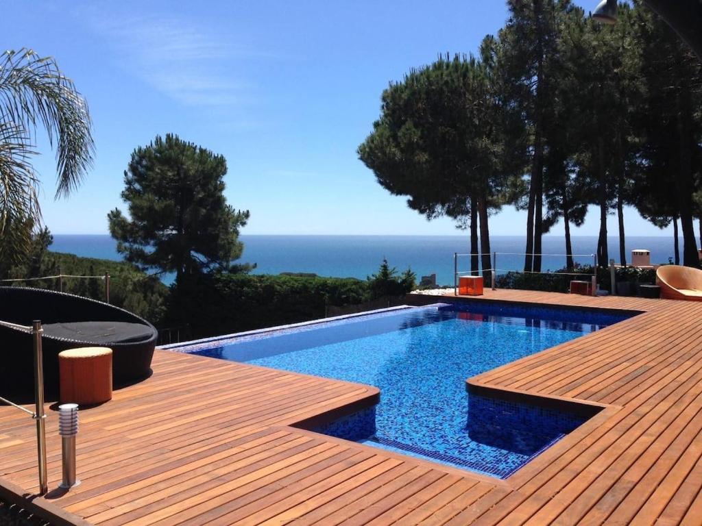 a swimming pool with a wooden deck and the ocean at Design villa with sea views in San Pol de Mar