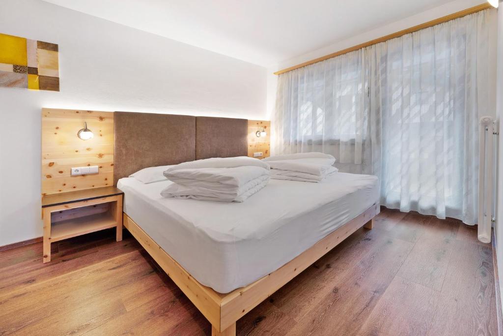 a bedroom with a bed with white sheets and a window at Apartments Antersi Claudia in San Vigilio Di Marebbe