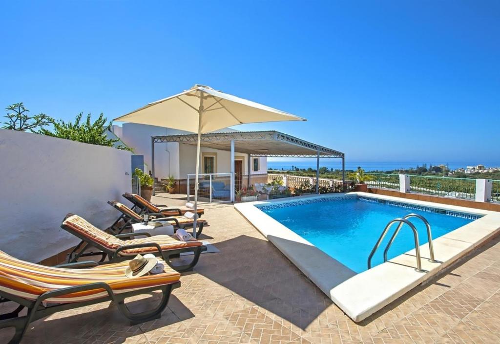 a villa with a swimming pool with chairs and an umbrella at El Puntal de Nieves in Nerja