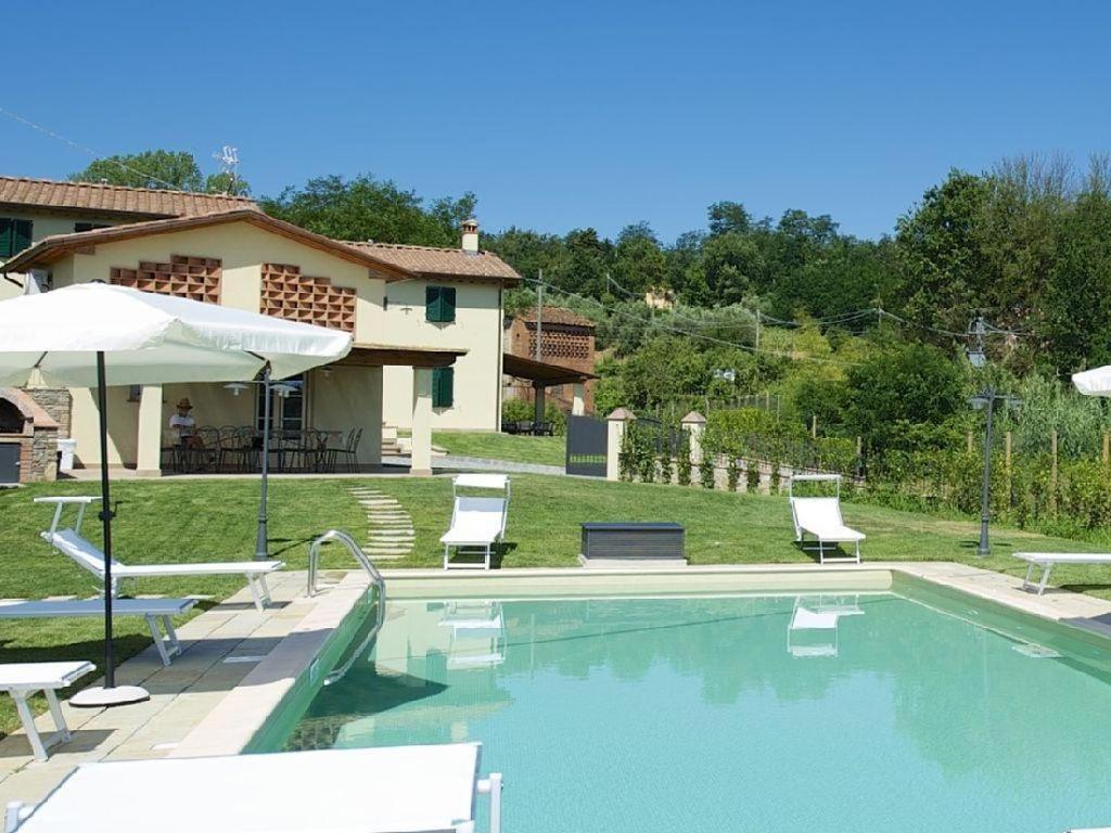 a swimming pool with chairs and an umbrella next to a house at Villa con piscina in Capannori