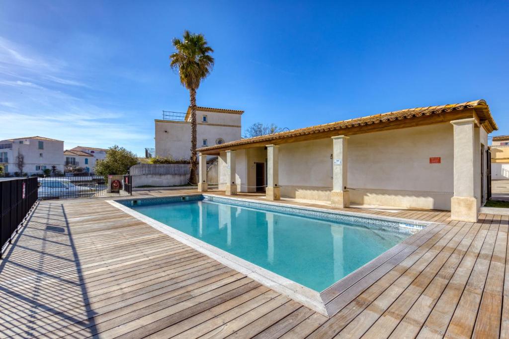 a swimming pool with a wooden deck and a house at Petite maison Aigues Mortes in Aigues-Mortes