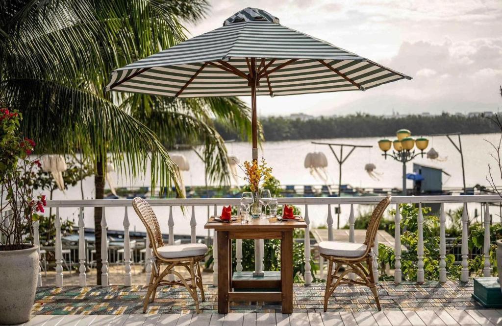 a table and chairs under an umbrella on a patio at CocoPalm Hoi An River Beach in Hoi An