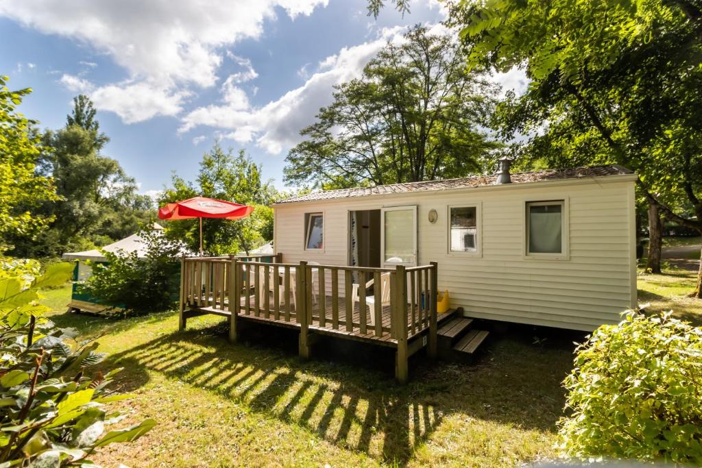 a white tiny house with a porch and a red umbrella at Mobilhome Le Tilleul in Saint-Pompont
