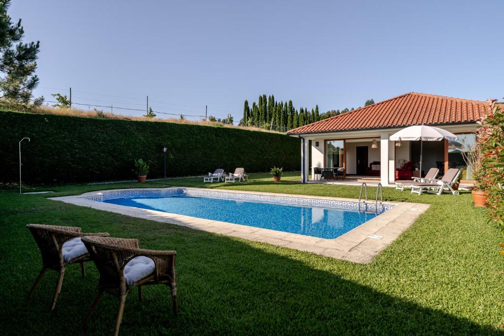 a swimming pool in a yard with two chairs and a house at Quinta do Outeirinho - Villa Deluxe in Celorico de Basto