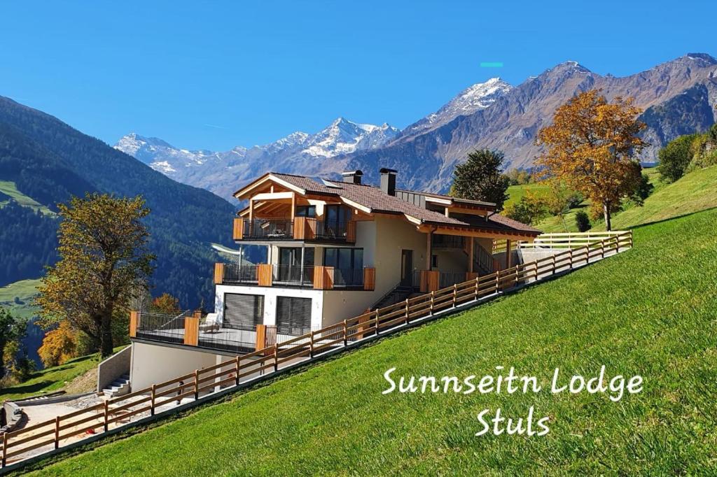 a house on a hill with mountains in the background at Sunnseitn Lodge Apartment Alps in Moso