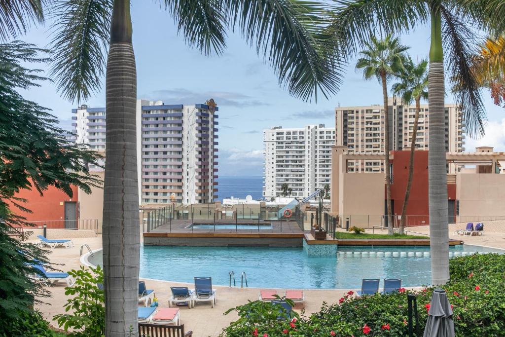 a swimming pool with palm trees and buildings at Palm Serenity in Playa Paraiso