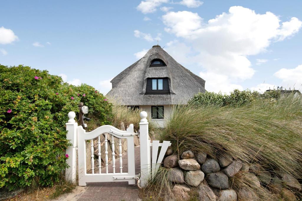 a house with a white gate and a thatch roof at Ferienwohnung Haus Lazy Dolphin in Rantum