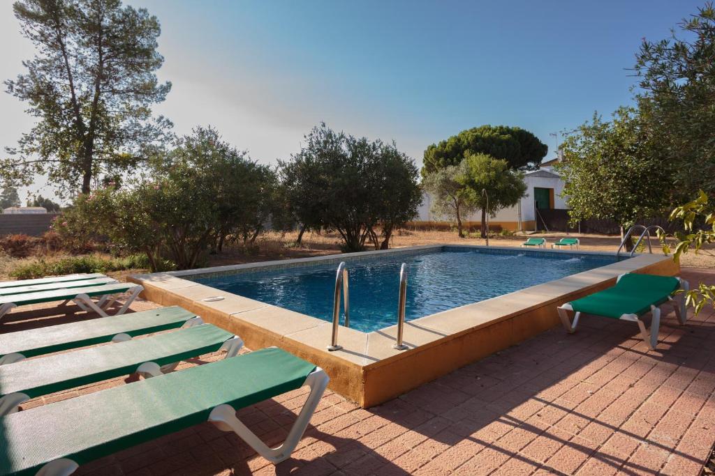 a swimming pool with two green benches next to it at Villa Los Pinos in Marchena
