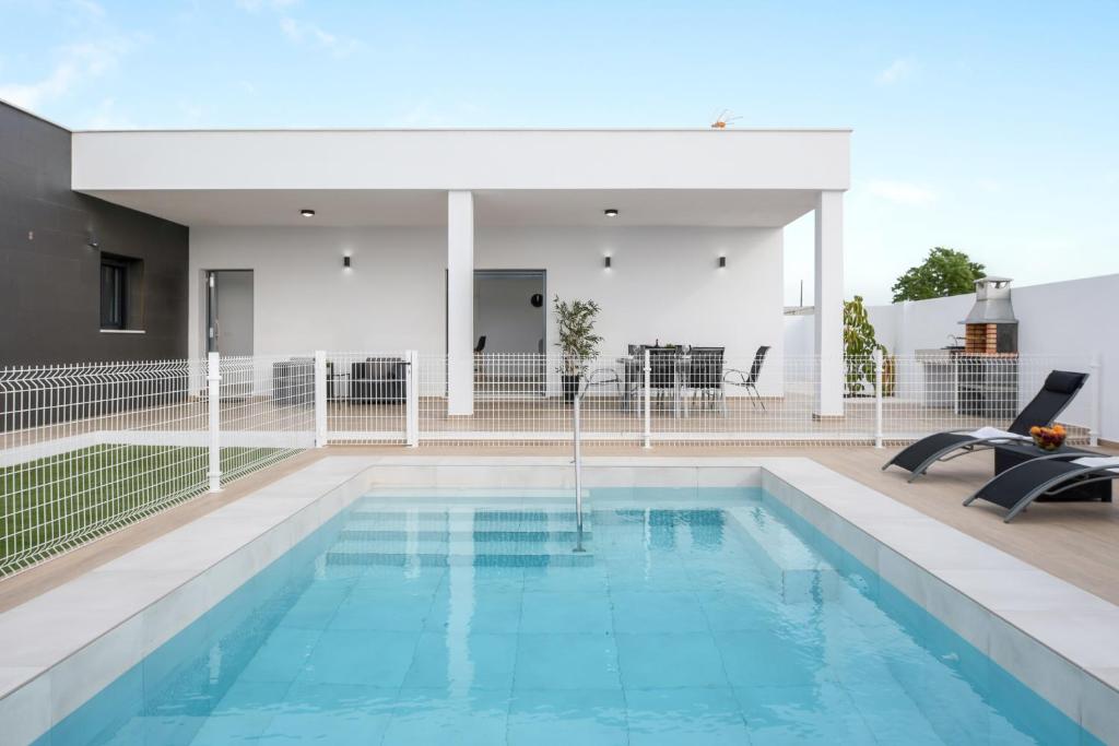 a swimming pool with two chairs in front of a building at Villa Sandra solo familias in Cádiz