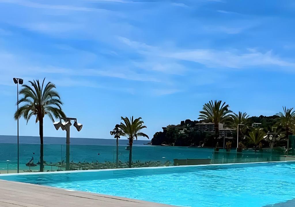 a swimming pool with palm trees and the ocean at First Line Mediterranean Apartment in Calvià