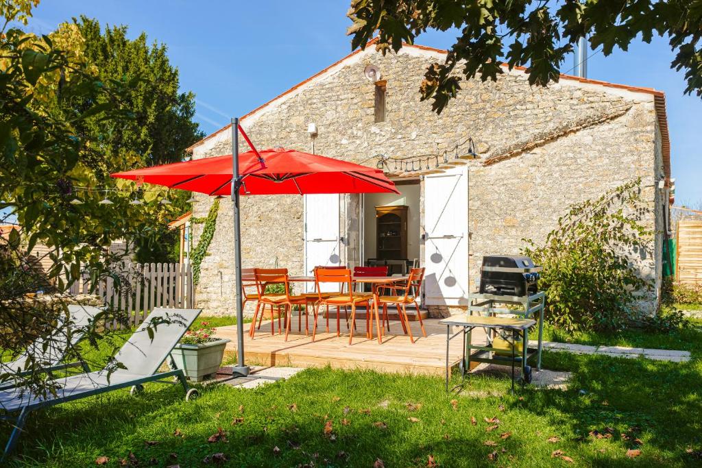 a patio with a table and a red umbrella at Gite La Grange Hulotte in Chaillé-les-Marais