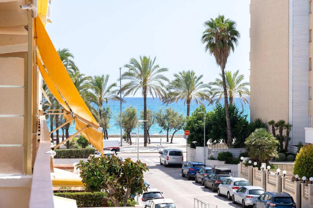 a street with parked cars and palm trees and the ocean at Calafenga in Calafell
