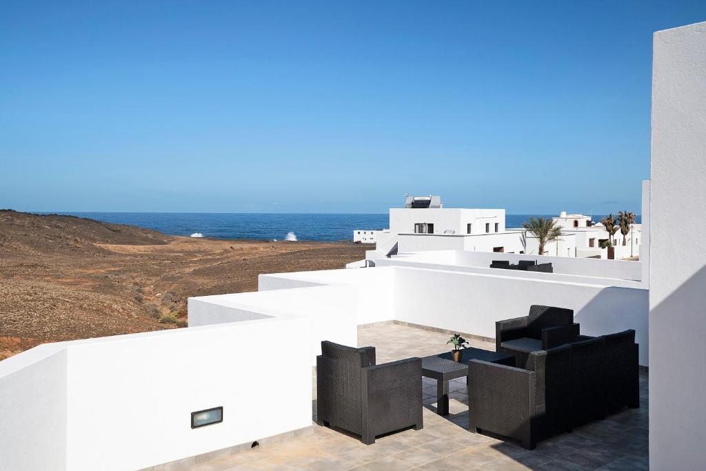 a white house with black chairs and the ocean at Tritón 6 in La Santa